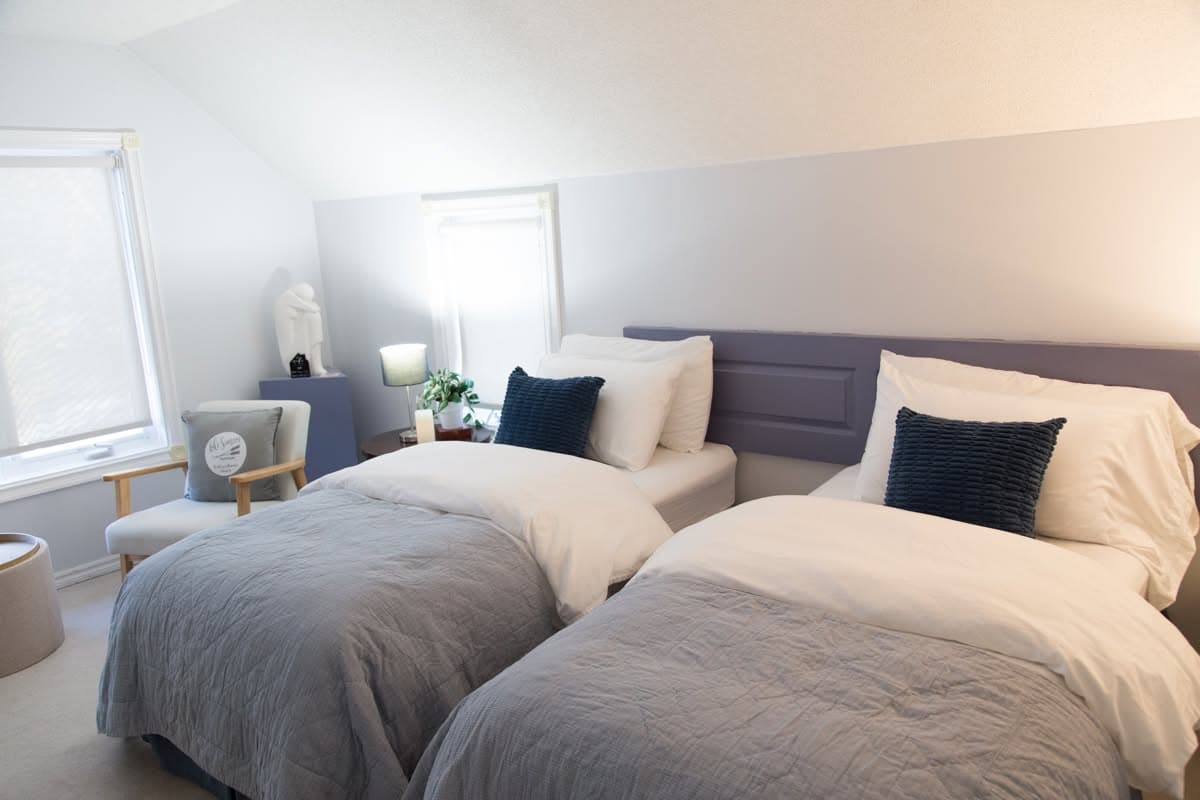 Two beds made up with soft grey quilts and navy cushions beneath a sloped attic ceiling