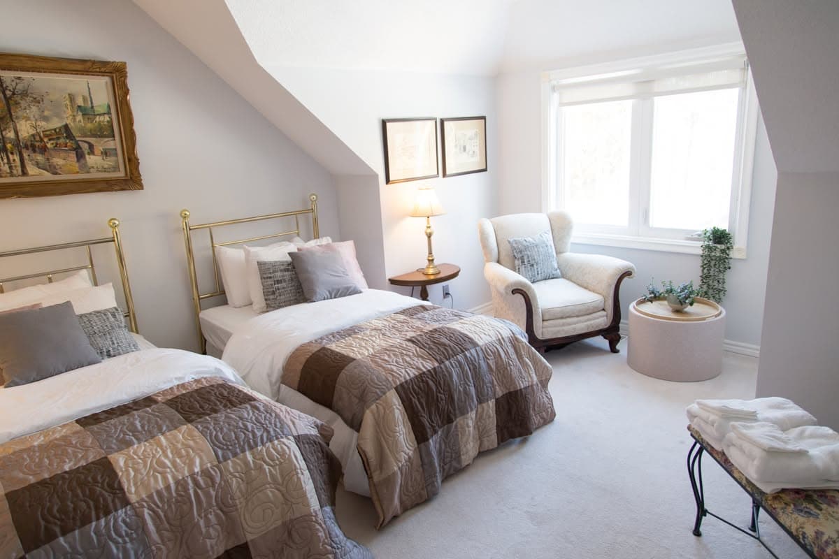Two brass bedsteads with patchwork quilts, a wingback armchair by the window