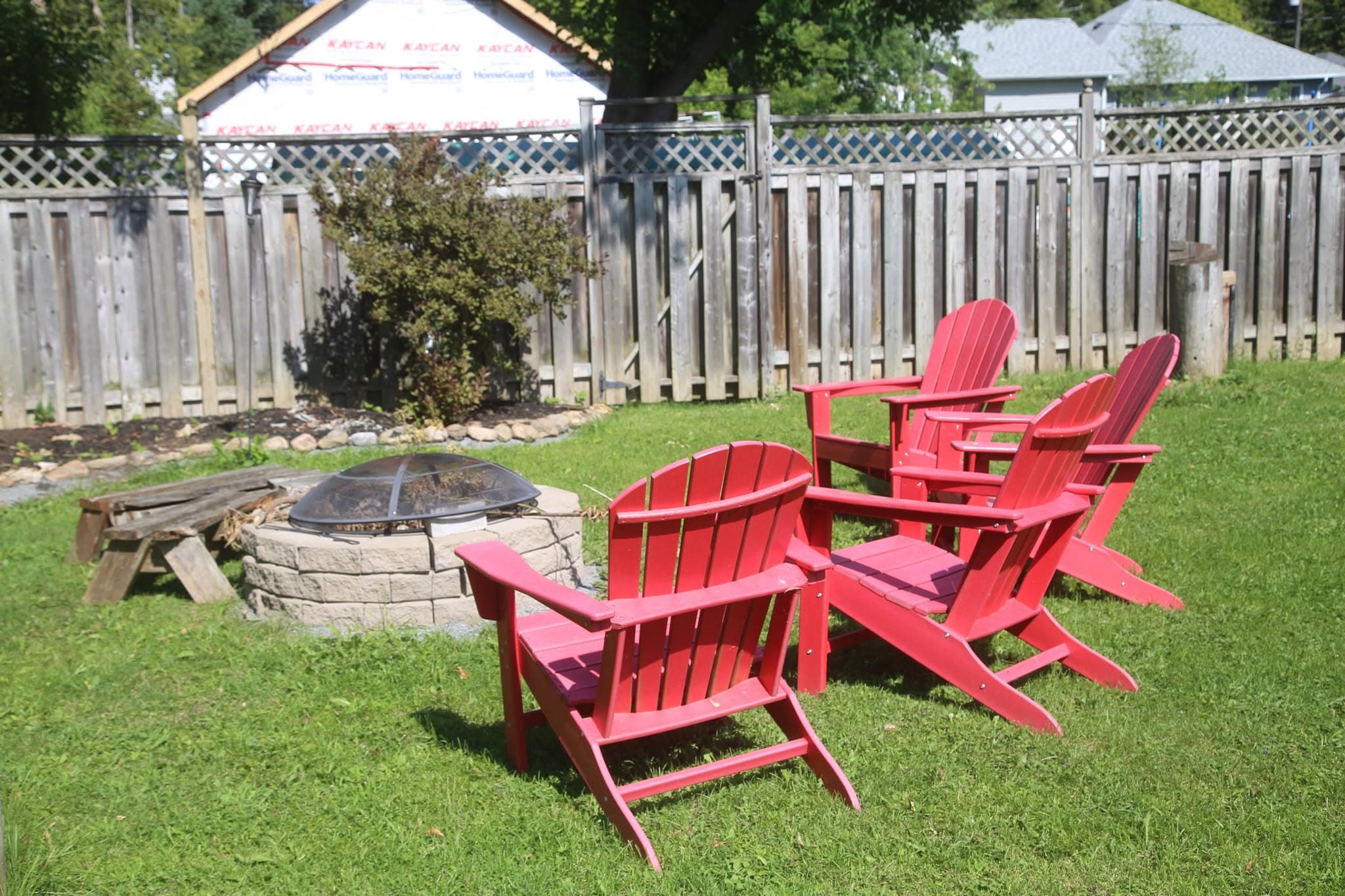 Stone fire pit with a stack of firewood and red chairs pulled up close