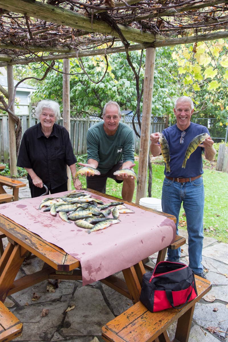 Three generations showing off a picnic table piled with fresh-caught perch under the pergola