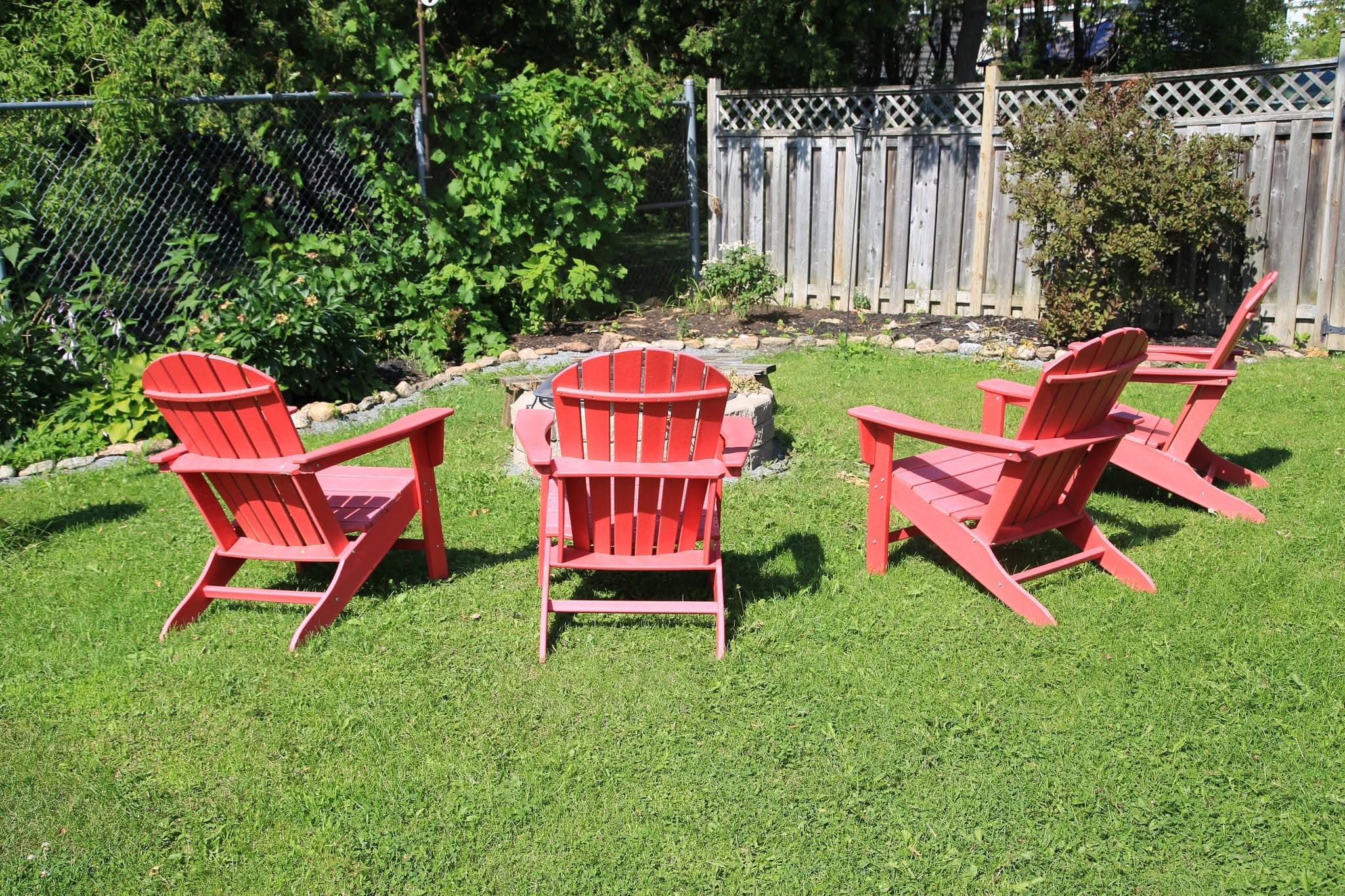 Red Muskoka chairs circled around the fire pit in the sunlit back garden
