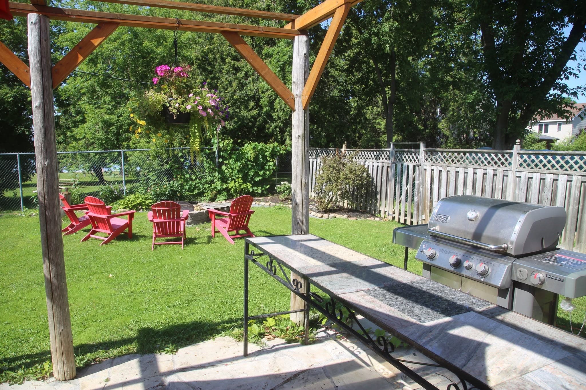 Timber pergola with hanging flower baskets and a barbecue, lawn and lake behind